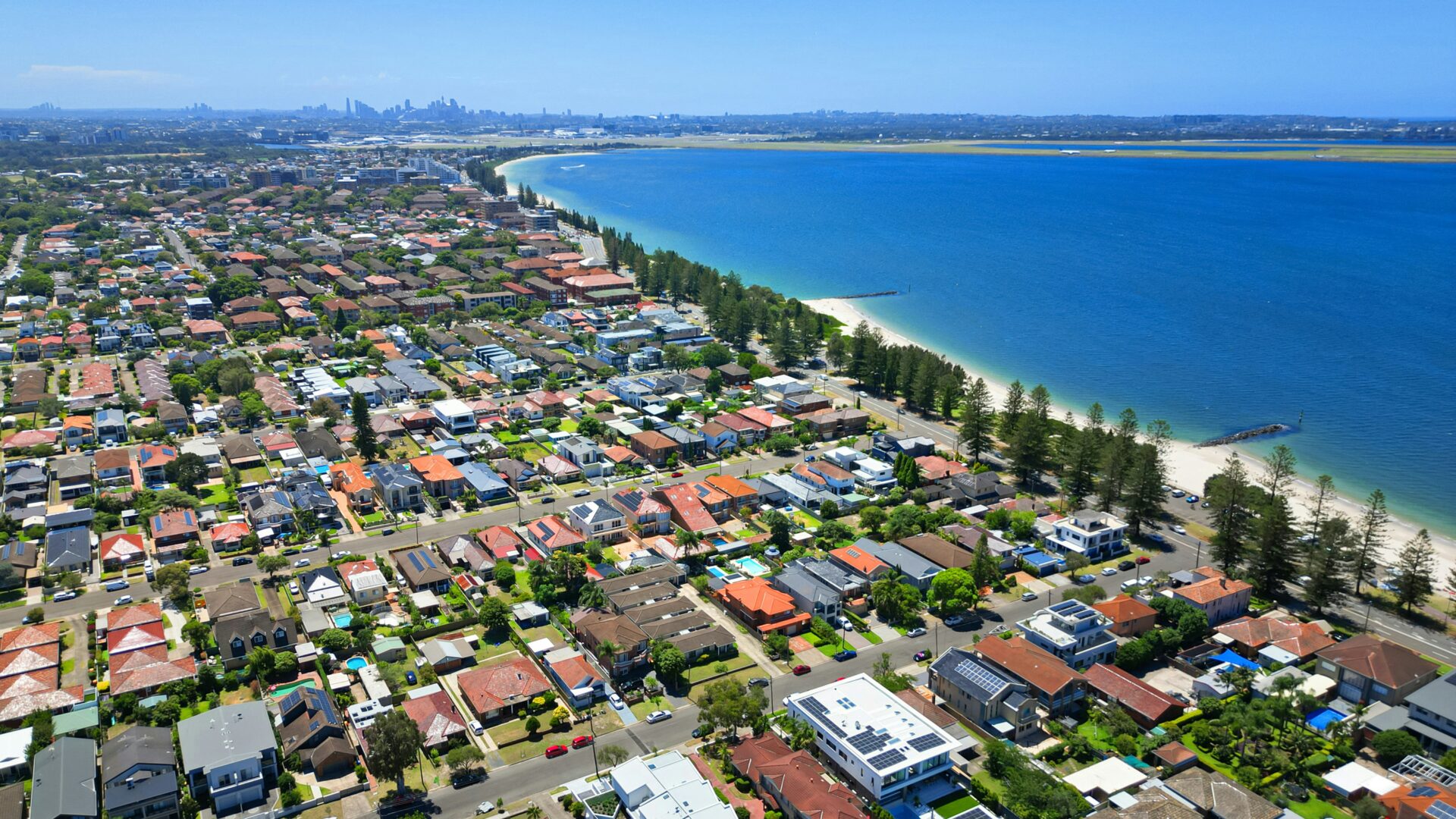 Australian Property Markets Show Historic Convergence as Growth Gaps Narrow to FourYear Low An aerial view of a coastal suburb in Australia, with houses and a beach next to the ocean.